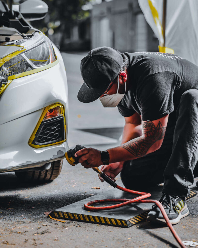 A man in a mask is sanding a scuffed bumper.