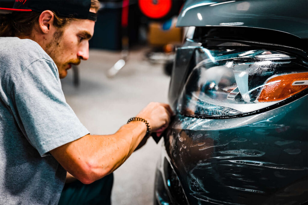 A man is applying Paint Protection Film to the headlight of a car.