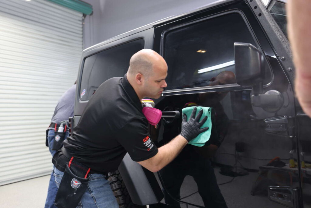 A man applying CK1 Ceramic Coatings to a black jeep in a garage.