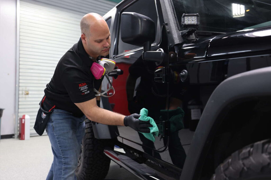 A man applying CK1 Ceramic Coatings to a black jeep in a garage.