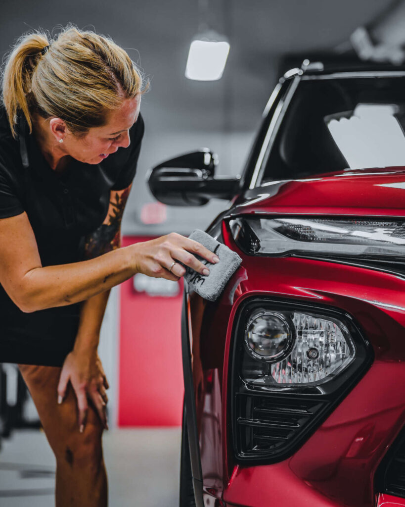 A woman receiving ceramic coating training on the hood of a red Toyota RAV4.