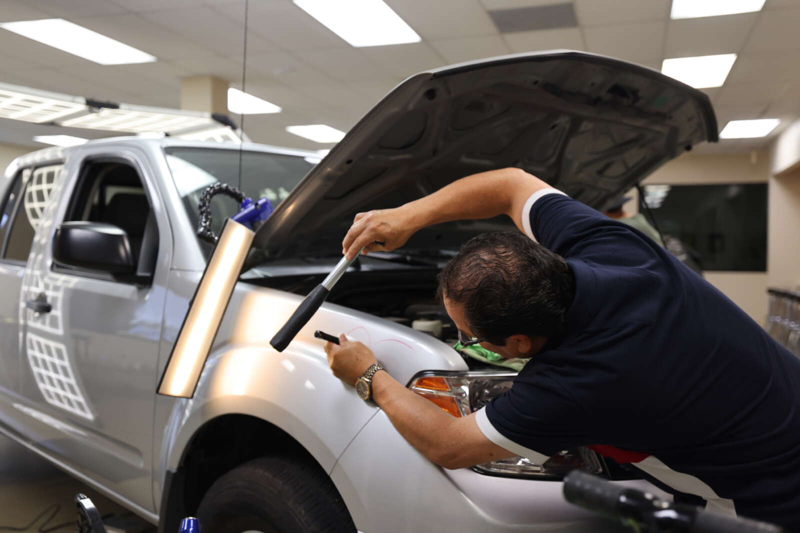 A man is training on the paintless dent repair technique while working on the fender of a car.