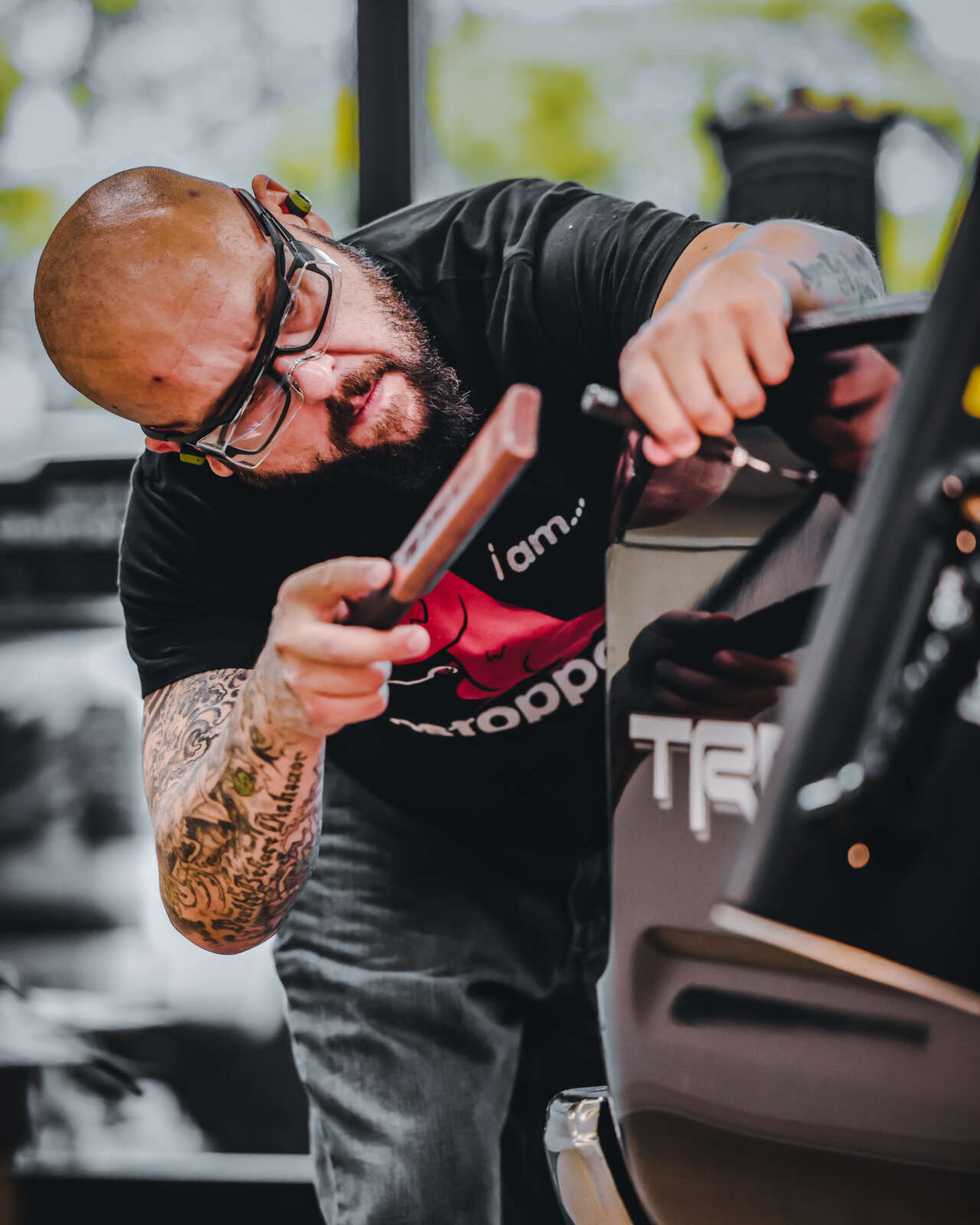 A tattooed man undergoing paintless dent repair training while working on a car.