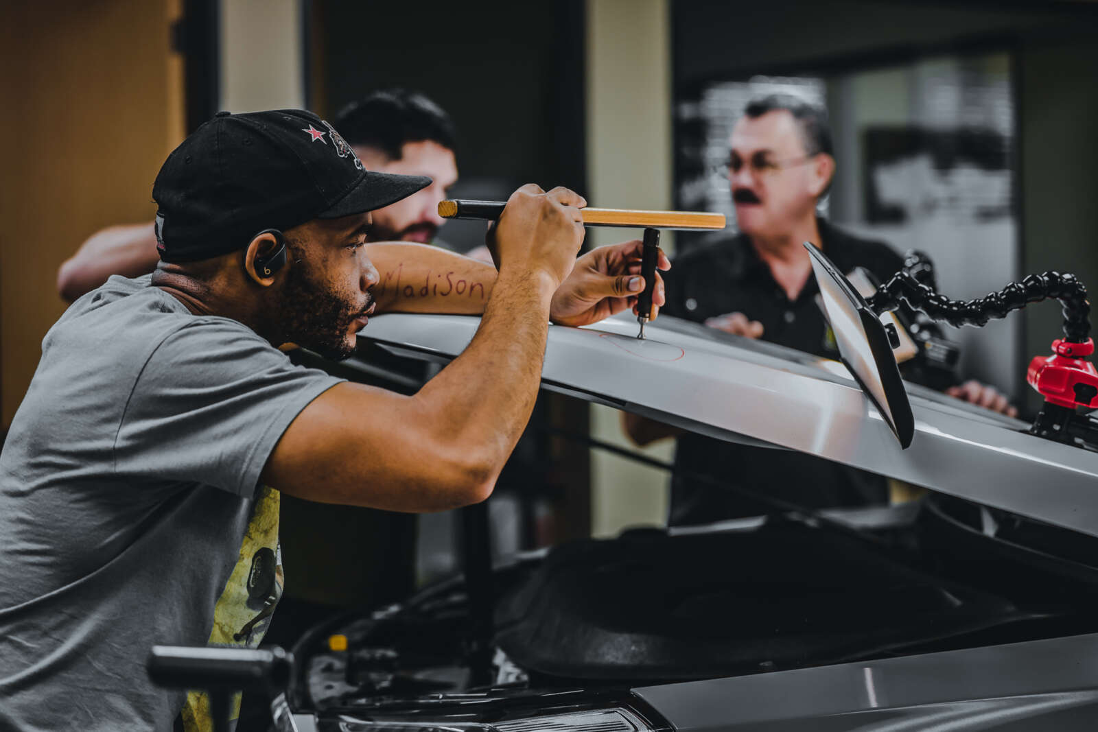 A man is receiving paintless dent repair training in a garage.