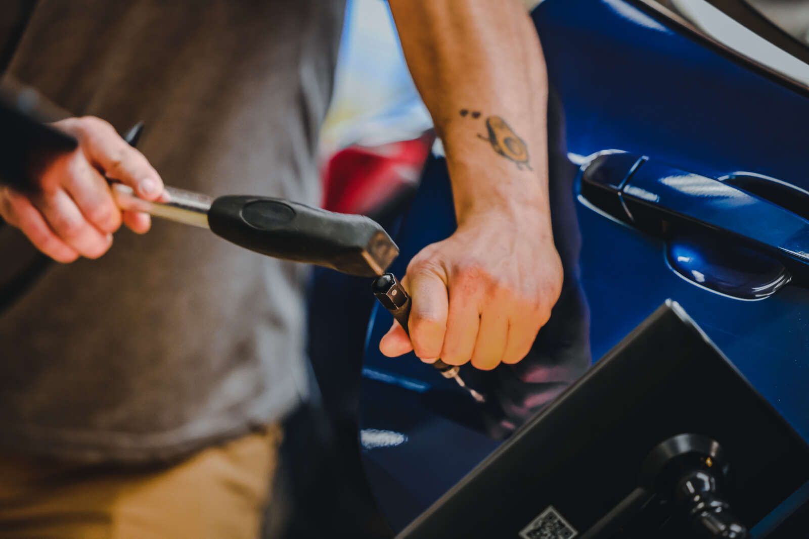 Student using a dent hammer to pound out a dent on a blue car door.