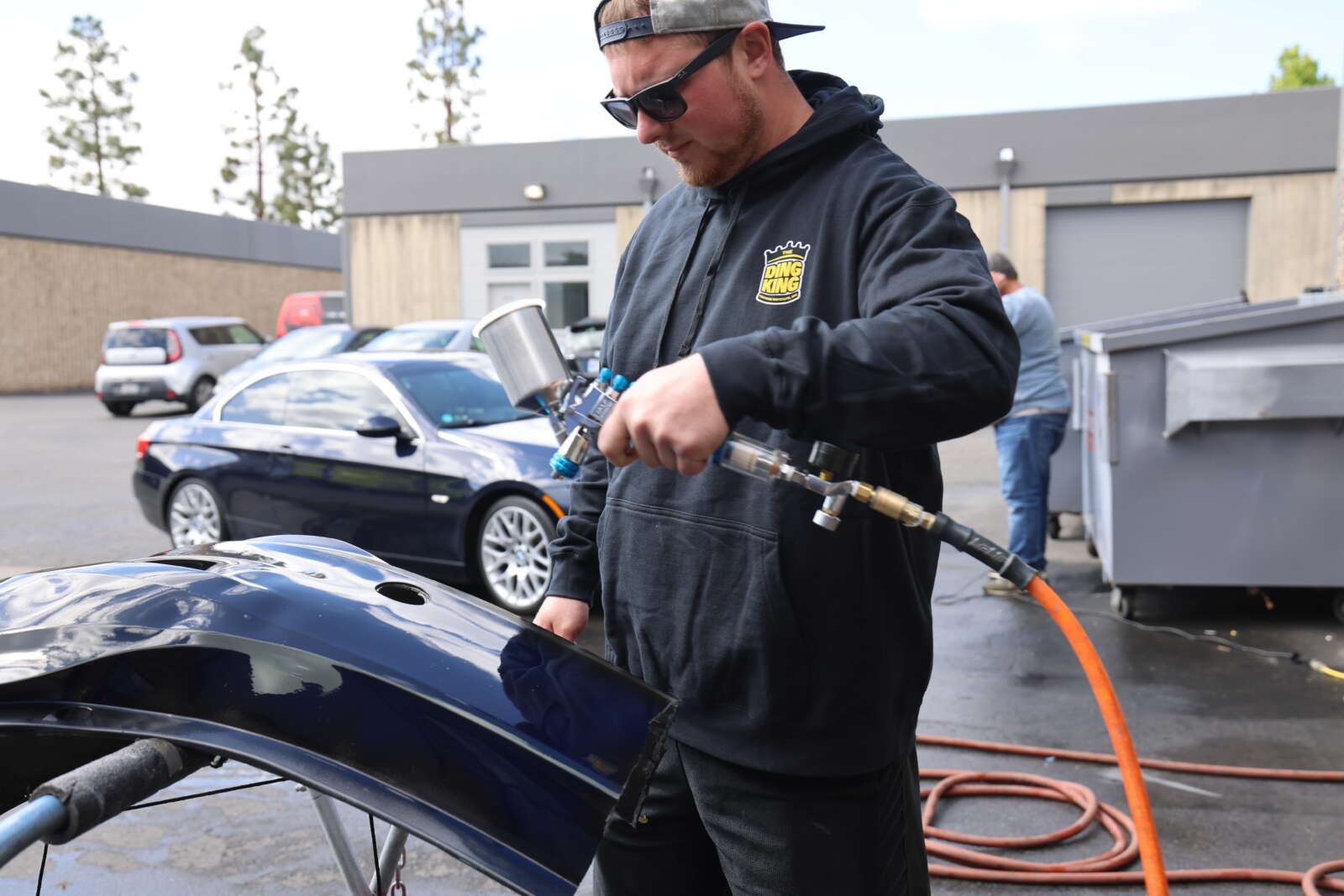 A man using a hose to blow off sanded areas on a repair of a scuffed bumper repair training.