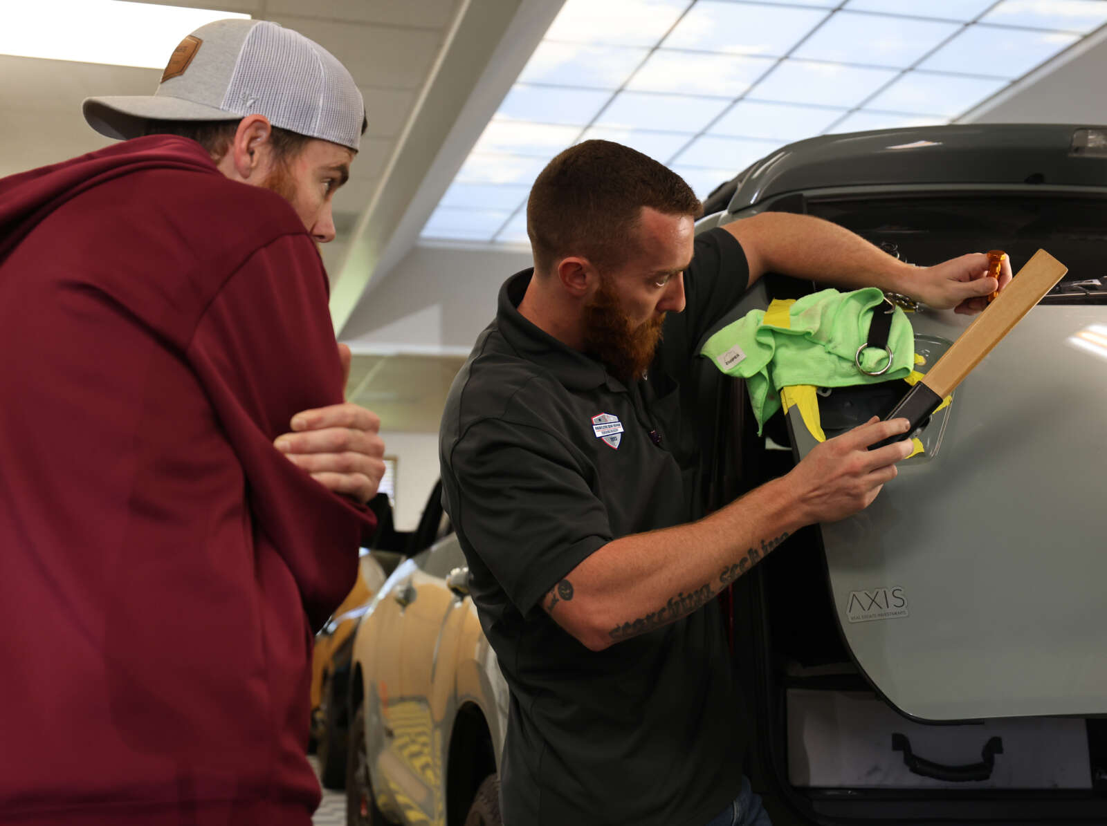 Instructor showing a student how to remove a dent on the hood of a vehicle.