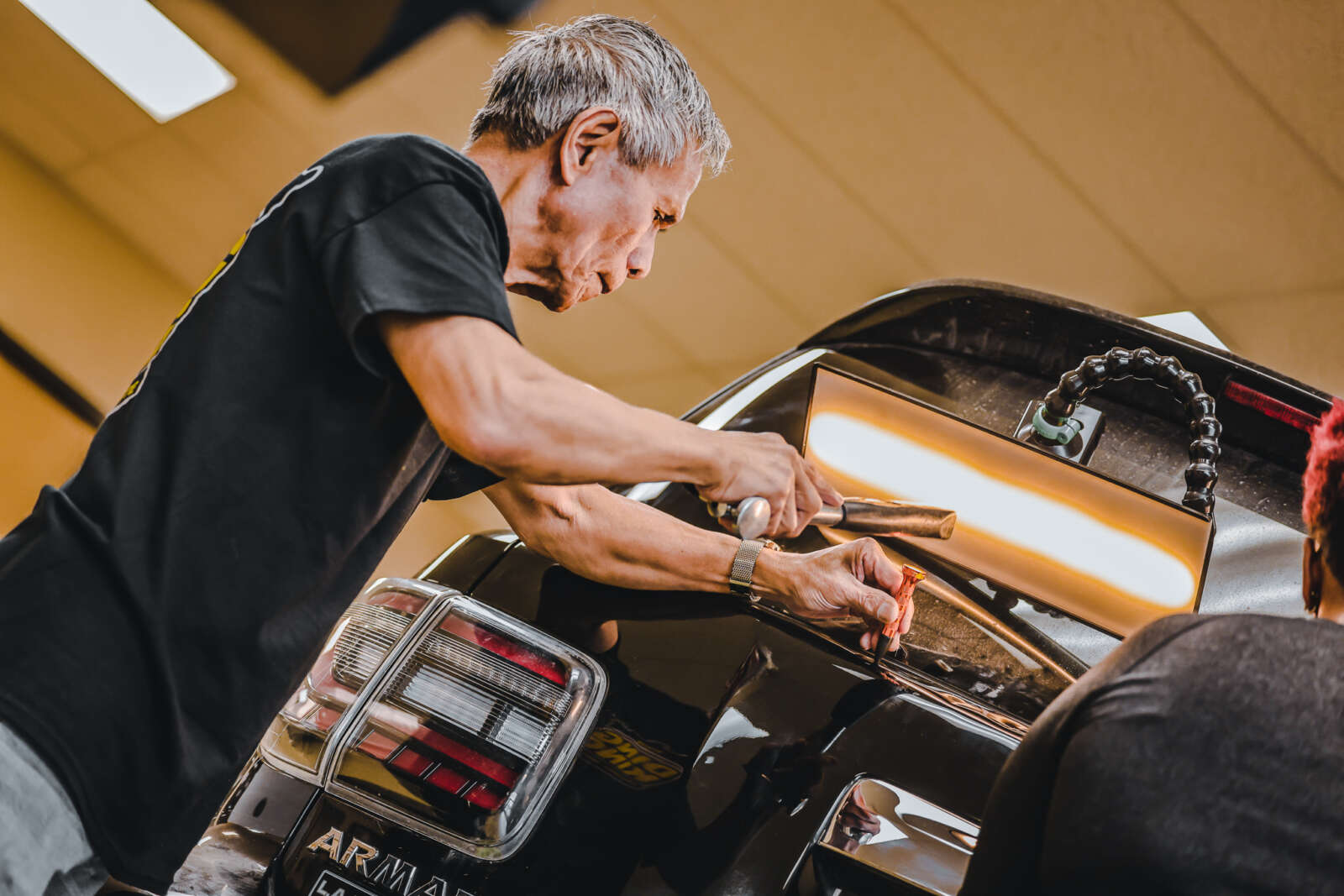 A man is receiving paintless dent repair training in a garage.