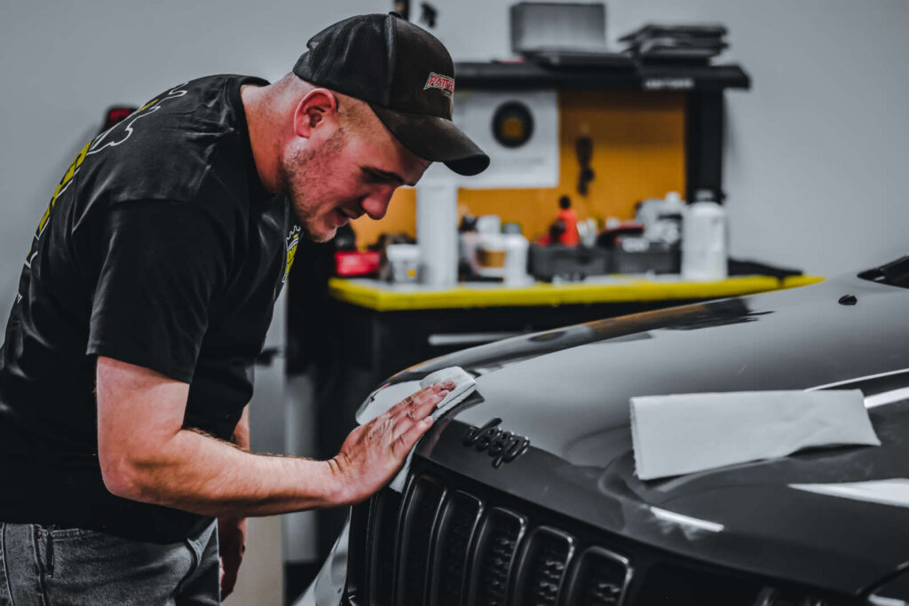 A man receiving paint chip repair training on a black hood of a jeep.