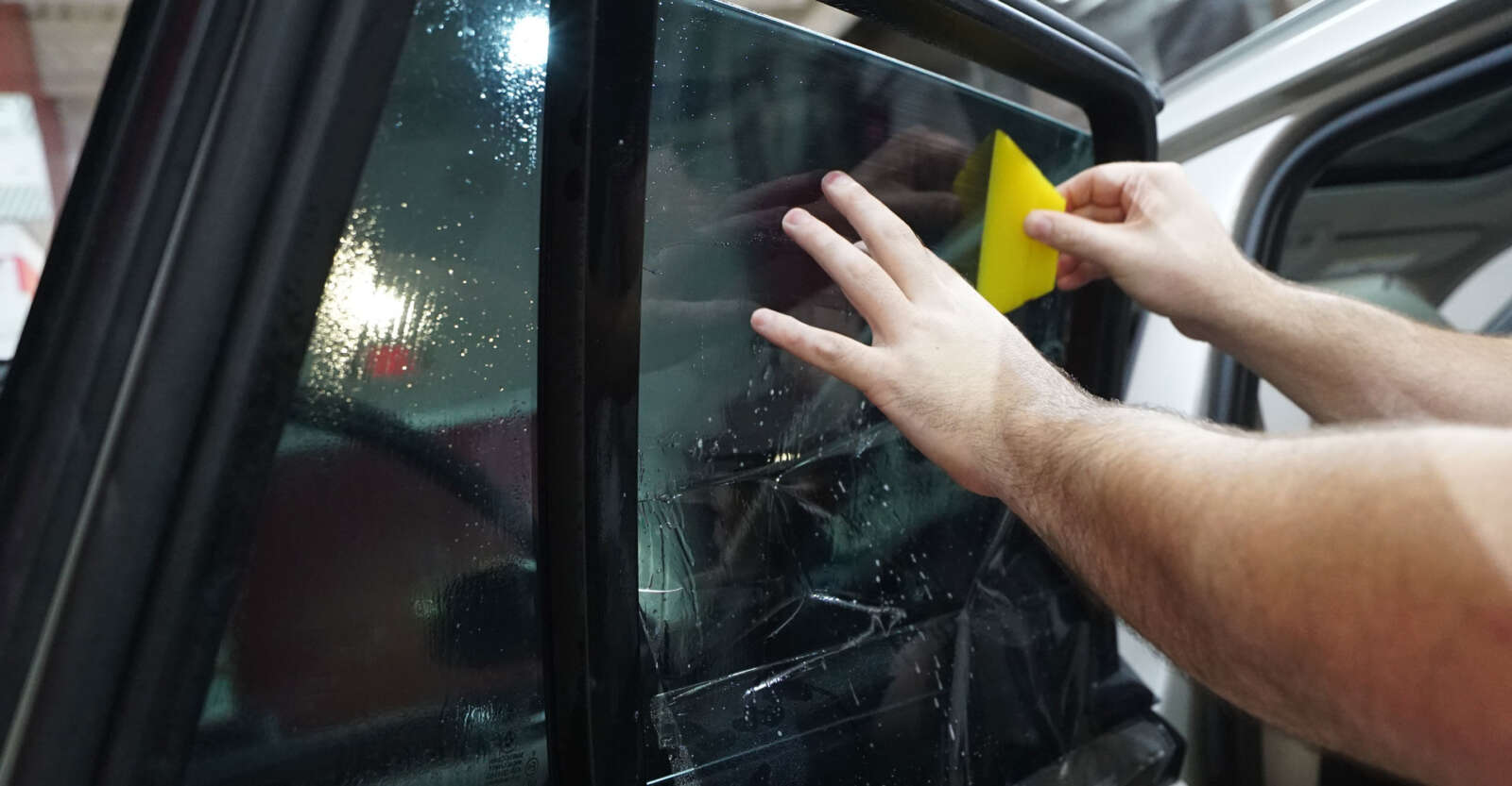 A man is applying a window tinting training to the window of a car as part of his window tinting training.