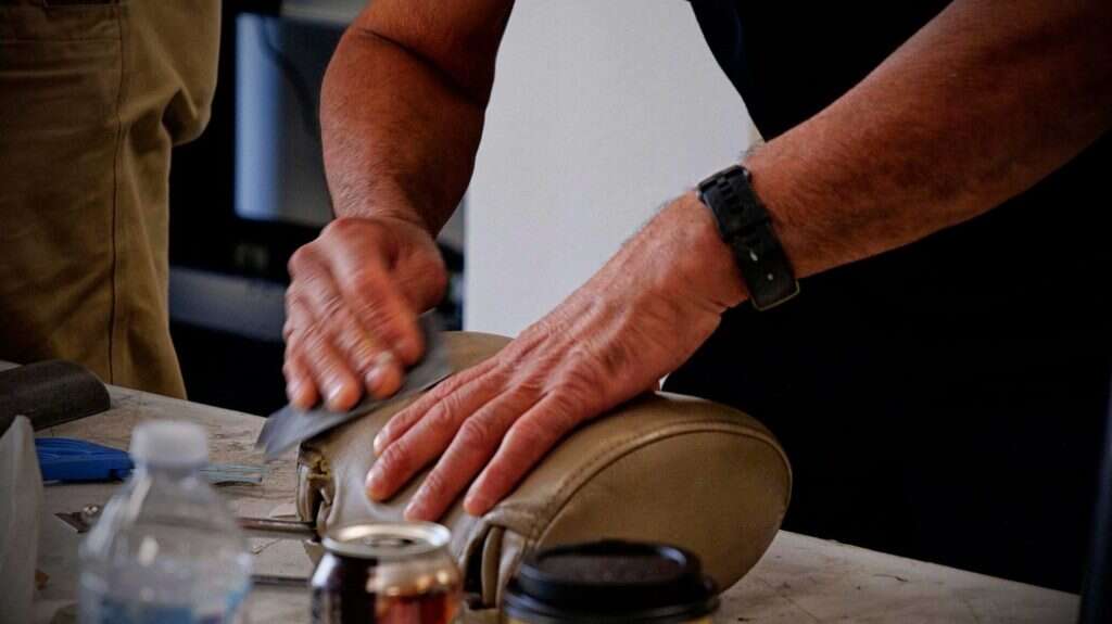 A man is sanding a leather head rest for interior repair training.